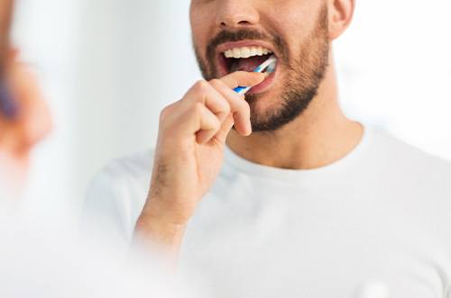 Nose-to-chest view of man in white t-shirt brushing teeth in front of mirror