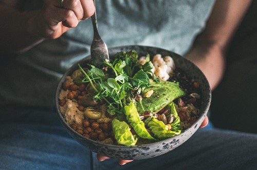 Hand forking salad from bowl in their lap