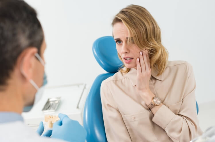 Woman holding cheek in pain before emergency dentistry