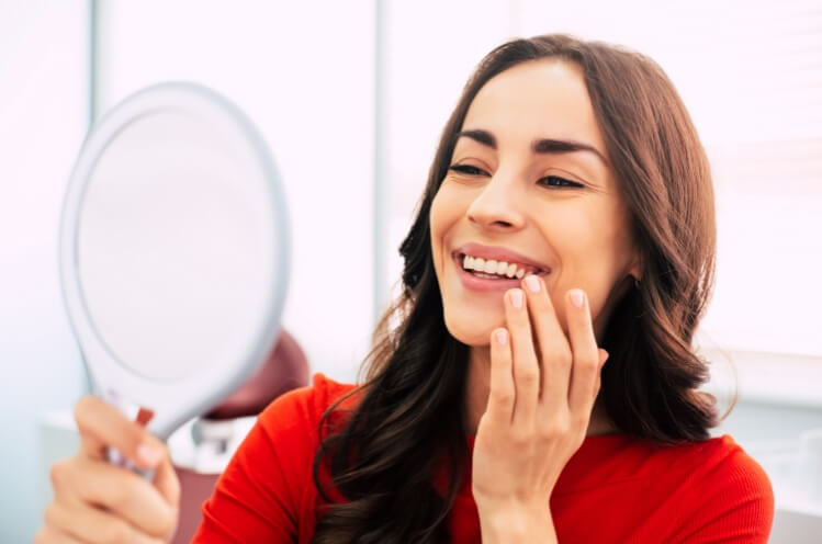 Woman looking at smile in mirror and enjoying the benefits of dental implants