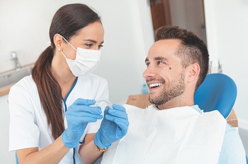 Dentist smiling at patient while holding Invisalign aligner 