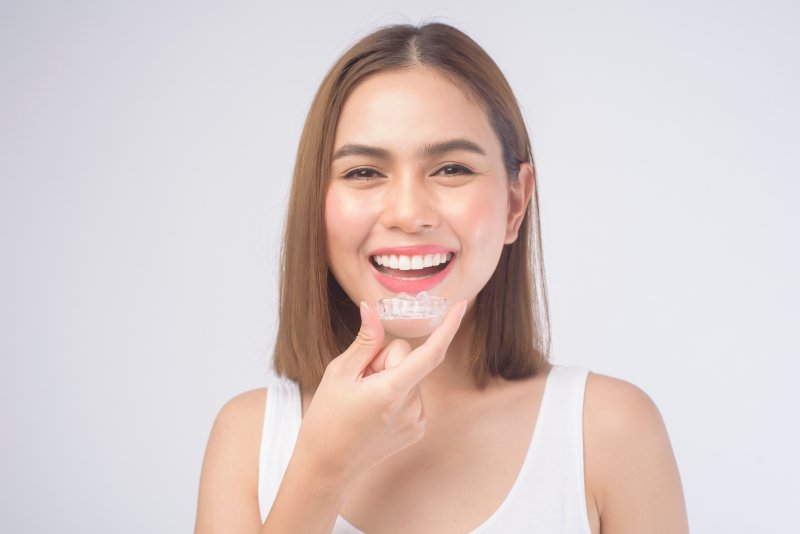 Young woman holding clear aligner up to her smile