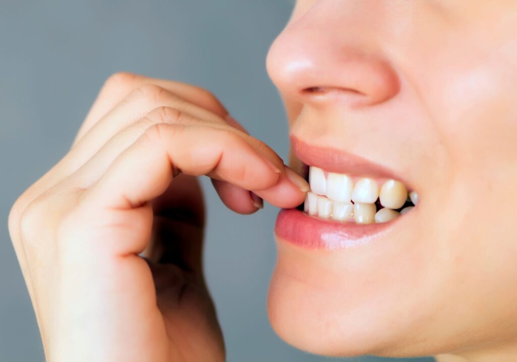 Nose-to-chin closeup of someone's teeth nibbling their fingernails
